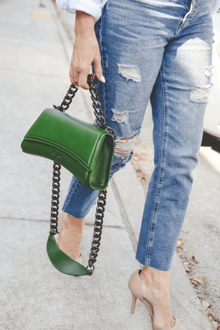 Close-up of an olive green leather handbag with a black chain strap on a white background.