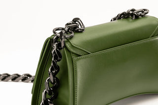 Close-up of an olive green leather handbag with a black chain strap on a white background.