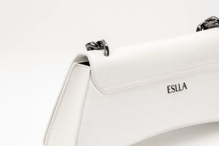 Close-up of a white leather handbag with a flap closure, black chain strap details.