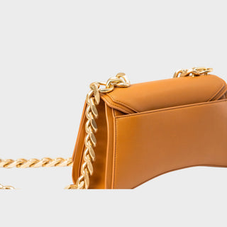 Close-up of a tan leather handbag with a gold chain strap on a light gray background.