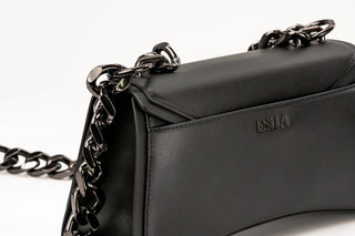 Close-up of a black leather shoulder bag with a dark gunmetal chain strap and an embossed ESLLA
