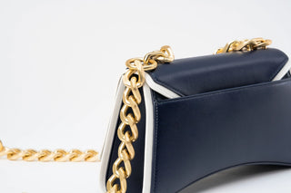 Close-up of a navy blue leather handbag with a chunky gold chain strap and white piping details
