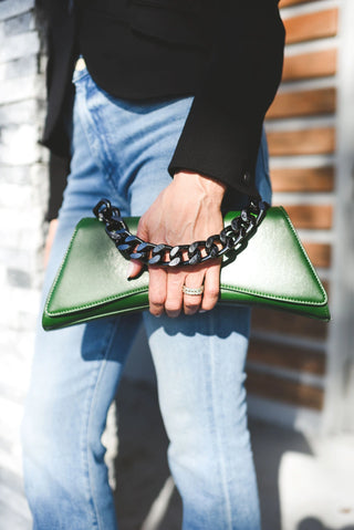 A person wearing blue jeans and a black top holds a green leather clutch bag