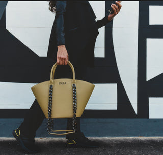 A person in a black blazer and black shoes carries a tan leather